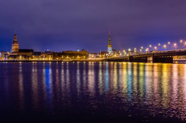 Gece görüşü tarihi şehir merkezine ve Daugava nehrinin kıyısındaki taştan köprüye sokak lambalarıyla renklendirilmiş Riga, Letonya