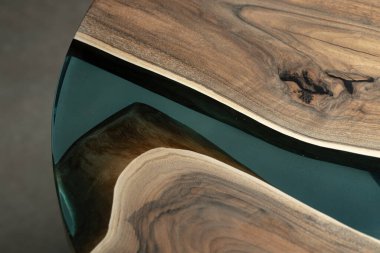 Pahalı eski mobilyalar. Masa epoksi reçineyle kaplanmış ve verniklenmiş. Lüks kaliteli ahşap işleme. Koyu arkaplanda tahta bir masa. Yuvarlak bir ağaç tablasında mavi bir epoksi nehri.