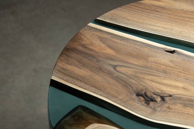 Pahalı eski mobilyalar. Masa epoksi reçineyle kaplanmış ve verniklenmiş. Lüks kaliteli ahşap işleme. Koyu arkaplanda tahta bir masa. Yuvarlak bir ağaç tablasında mavi bir epoksi nehri.