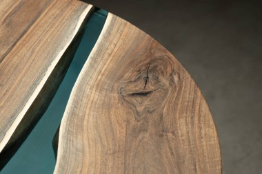 Pahalı eski mobilyalar. Masa epoksi reçineyle kaplanmış ve verniklenmiş. Lüks kaliteli ahşap işleme. Koyu arkaplanda tahta bir masa. Yuvarlak bir ağaç tablasında mavi bir epoksi nehri.