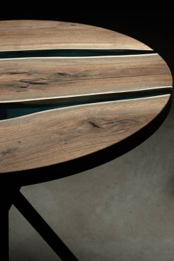 Pahalı eski mobilyalar. Masa epoksi reçineyle kaplanmış ve verniklenmiş. Lüks kaliteli ahşap işleme. Koyu arkaplanda tahta bir masa. Yuvarlak bir ağaç tablasında mavi bir epoksi nehri.