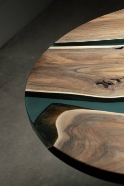 Pahalı eski mobilyalar. Masa epoksi reçineyle kaplanmış ve verniklenmiş. Lüks kaliteli ahşap işleme. Koyu arkaplanda tahta bir masa. Yuvarlak bir ağaç tablasında mavi bir epoksi nehri.