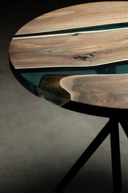 Pahalı eski mobilyalar. Masa epoksi reçineyle kaplanmış ve verniklenmiş. Lüks kaliteli ahşap işleme. Koyu arkaplanda tahta bir masa. Yuvarlak bir ağaç tablasında mavi bir epoksi nehri.