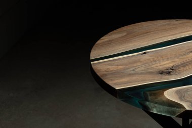 Pahalı eski mobilyalar. Masa epoksi reçineyle kaplanmış ve verniklenmiş. Lüks kaliteli ahşap işleme. Koyu arkaplanda tahta bir masa. Yuvarlak bir ağaç tablasında mavi bir epoksi nehri.