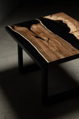 Pahalı eski mobilyalar. Masa epoksi reçineyle kaplanmış ve verniklenmiş. Lüks kaliteli ahşap işleme. Beton zeminde tahta bir masa. Dikdörtgen bir ağaç tabakasında siyah bir epoksi nehri..