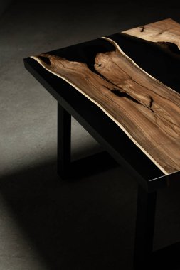 Pahalı eski mobilyalar. Masa epoksi reçineyle kaplanmış ve verniklenmiş. Lüks kaliteli ahşap işleme. Beton zeminde tahta bir masa. Dikdörtgen bir ağaç tabakasında siyah bir epoksi nehri..
