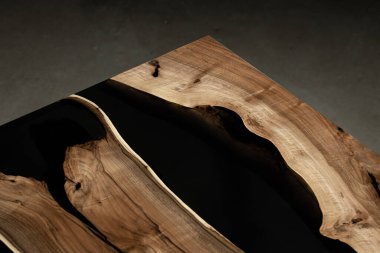 Pahalı eski mobilyalar. Masa epoksi reçineyle kaplanmış ve verniklenmiş. Lüks kaliteli ahşap işleme. Beton zeminde tahta bir masa. Dikdörtgen bir ağaç tabakasında siyah bir epoksi nehri..