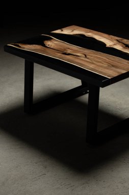 Pahalı eski mobilyalar. Masa epoksi reçineyle kaplanmış ve verniklenmiş. Lüks kaliteli ahşap işleme. Beton zeminde tahta bir masa. Dikdörtgen bir ağaç tabakasında siyah bir epoksi nehri..