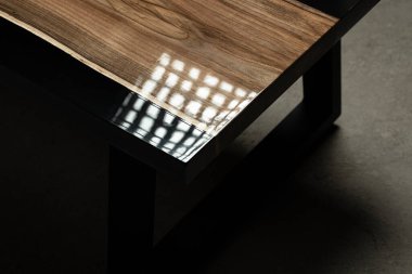 Pahalı eski mobilyalar. Masa epoksi reçineyle kaplanmış ve verniklenmiş. Lüks kaliteli ahşap işleme. Beton zeminde tahta bir masa. Dikdörtgen bir ağaç tabakasında siyah bir epoksi nehri..