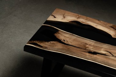 Pahalı eski mobilyalar. Masa epoksi reçineyle kaplanmış ve verniklenmiş. Lüks kaliteli ahşap işleme. Beton zeminde tahta bir masa. Dikdörtgen bir ağaç tabakasında siyah bir epoksi nehri..