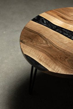 Pahalı eski mobilyalar. Masa epoksi reçineyle kaplanmış ve verniklenmiş. Lüks kaliteli ahşap işleme. Koyu arkaplanda tahta bir masa. Yuvarlak bir ağaç tablasında siyah bir epoksi nehri.