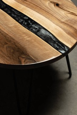 Pahalı eski mobilyalar. Masa epoksi reçineyle kaplanmış ve verniklenmiş. Lüks kaliteli ahşap işleme. Koyu arkaplanda tahta bir masa. Yuvarlak bir ağaç tablasında siyah bir epoksi nehri.