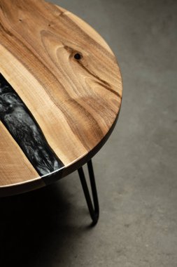 Pahalı eski mobilyalar. Masa epoksi reçineyle kaplanmış ve verniklenmiş. Lüks kaliteli ahşap işleme. Koyu arkaplanda tahta bir masa. Yuvarlak bir ağaç tablasında siyah bir epoksi nehri.