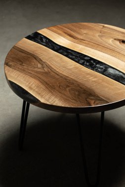 Pahalı eski mobilyalar. Masa epoksi reçineyle kaplanmış ve verniklenmiş. Lüks kaliteli ahşap işleme. Koyu arkaplanda tahta bir masa. Yuvarlak bir ağaç tablasında siyah bir epoksi nehri.