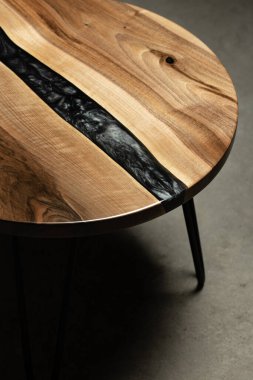 Pahalı eski mobilyalar. Masa epoksi reçineyle kaplanmış ve verniklenmiş. Lüks kaliteli ahşap işleme. Koyu arkaplanda tahta bir masa. Yuvarlak bir ağaç tablasında siyah bir epoksi nehri.