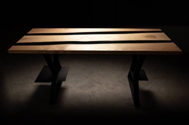 Pahalı eski mobilyalar. Masa epoksi reçineyle kaplanmış ve verniklenmiş. Lüks kaliteli ahşap işleme. Koyu arkaplanda tahta bir masa. Bir bilgisayar masası için donanım.