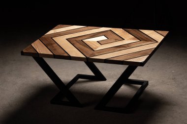 Pahalı eski mobilyalar. Masa epoksi reçineyle kaplanmış ve verniklenmiş. Lüks kaliteli ahşap işleme. Koyu arkaplanda tahta bir masa. Labirent şeklinde dönen geometrik desenler.