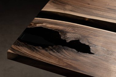 Pahalı eski mobilyalar. Masa epoksi reçineyle kaplanmış ve verniklenmiş. Lüks kaliteli ahşap işleme. Koyu arkaplanda tahta bir masa. Yuvarlak bir ağaç tablasında siyah bir epoksi nehri.