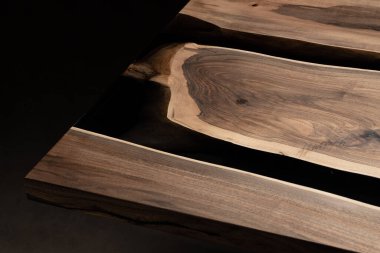 Pahalı eski mobilyalar. Masa epoksi reçineyle kaplanmış ve verniklenmiş. Lüks kaliteli ahşap işleme. Koyu arkaplanda tahta bir masa. Yuvarlak bir ağaç tablasında siyah bir epoksi nehri.