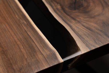 Pahalı eski mobilyalar. Masa epoksi reçineyle kaplanmış ve verniklenmiş. Lüks kaliteli ahşap işleme. Koyu arkaplanda tahta bir masa. Yuvarlak bir ağaç tablasında siyah bir epoksi nehri.