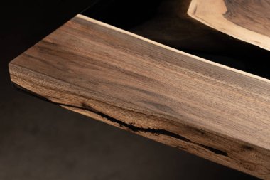 Pahalı eski mobilyalar. Masa epoksi reçineyle kaplanmış ve verniklenmiş. Lüks kaliteli ahşap işleme. Koyu arkaplanda tahta bir masa. Yuvarlak bir ağaç tablasında siyah bir epoksi nehri.