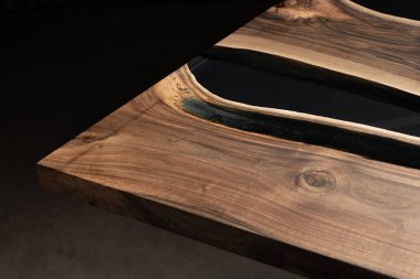 Pahalı eski mobilyalar. Masa epoksi reçineyle kaplanmış ve verniklenmiş. Lüks kaliteli ahşap işleme. Koyu arkaplanda tahta bir masa. Yuvarlak bir ağaç tablasında siyah bir epoksi nehri.