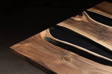 Pahalı eski mobilyalar. Masa epoksi reçineyle kaplanmış ve verniklenmiş. Lüks kaliteli ahşap işleme. Koyu arkaplanda tahta bir masa. Yuvarlak bir ağaç tablasında siyah bir epoksi nehri.