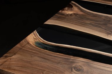 Pahalı eski mobilyalar. Masa epoksi reçineyle kaplanmış ve verniklenmiş. Lüks kaliteli ahşap işleme. Koyu arkaplanda tahta bir masa. Yuvarlak bir ağaç tablasında siyah bir epoksi nehri.