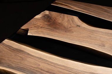 Pahalı eski mobilyalar. Masa epoksi reçineyle kaplanmış ve verniklenmiş. Lüks kaliteli ahşap işleme. Koyu arkaplanda tahta bir masa. Yuvarlak bir ağaç tablasında siyah bir epoksi nehri.