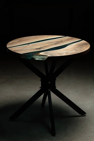 Pahalı eski mobilyalar. Masa epoksi reçineyle kaplanmış ve verniklenmiş. Lüks kaliteli ahşap işleme. Koyu arkaplanda tahta bir masa. Yuvarlak bir ağaç tablasında mavi bir epoksi nehri.