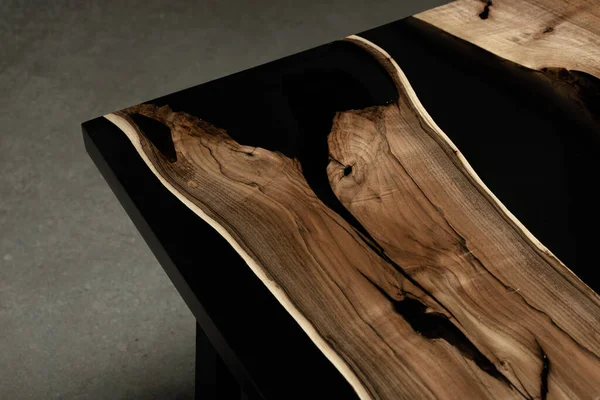 Pahalı eski mobilyalar. Masa epoksi reçineyle kaplanmış ve verniklenmiş. Lüks kaliteli ahşap işleme. Beton zeminde tahta bir masa. Dikdörtgen bir ağaç tabakasında siyah bir epoksi nehri..