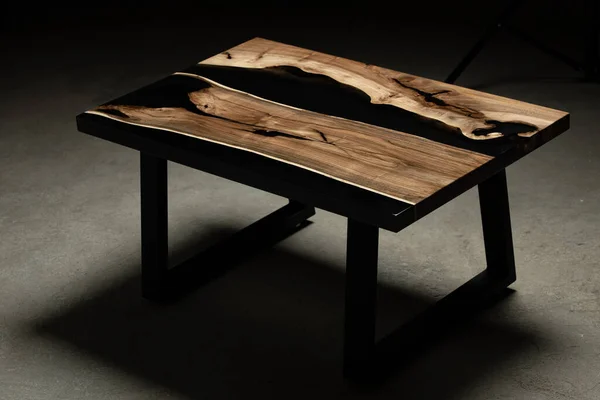 Pahalı eski mobilyalar. Masa epoksi reçineyle kaplanmış ve verniklenmiş. Lüks kaliteli ahşap işleme. Beton zeminde tahta bir masa. Dikdörtgen bir ağaç tabakasında siyah bir epoksi nehri..