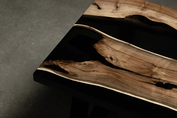 Pahalı eski mobilyalar. Masa epoksi reçineyle kaplanmış ve verniklenmiş. Lüks kaliteli ahşap işleme. Beton zeminde tahta bir masa. Dikdörtgen bir ağaç tabakasında siyah bir epoksi nehri..