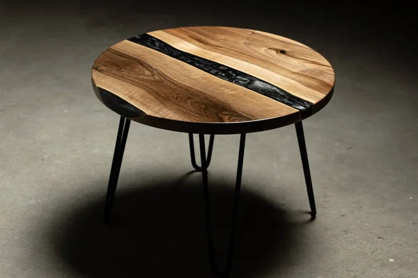 Pahalı eski mobilyalar. Masa epoksi reçineyle kaplanmış ve verniklenmiş. Lüks kaliteli ahşap işleme. Koyu arkaplanda tahta bir masa. Yuvarlak bir ağaç tablasında siyah bir epoksi nehri.