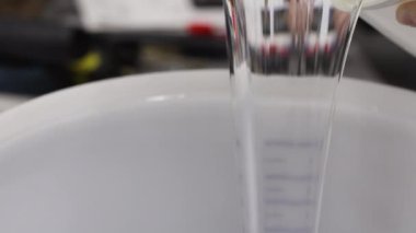 Epoksi reçine bileşenlerini boyayla karıştırıyorum. Özel mobilya imalatının aşamalarından biri. Lüks kaliteli ahşap işleme. Sıvıyı bir konteynırdan diğerine aktarmak.