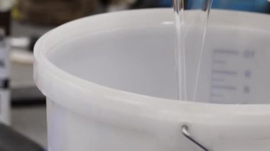 Epoksi reçine bileşenlerini boyayla karıştırıyorum. Özel mobilya imalatının aşamalarından biri. Lüks kaliteli ahşap işleme. Sıvıyı bir konteynırdan diğerine aktarmak.