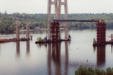 Nehrin üzerindeki beton köprü. Karmaşık teknik projeler. Büyük bir mimari yapı yapım aşamasında. Sütunların inşası için geçici demir yığınları. Büyük endüstriyel ekipman.