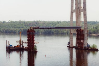 Concrete bridge over the river. Complex technical projects. A large architectural structure under construction. Temporary iron piles for the construction of columns. Large industrial equipment.