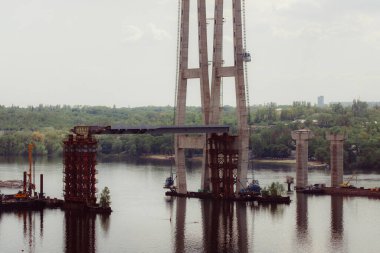 Nehrin üzerindeki beton köprü. Karmaşık teknik projeler. Büyük bir mimari yapı yapım aşamasında. Sütunların inşası için geçici demir yığınları. Büyük endüstriyel ekipman.