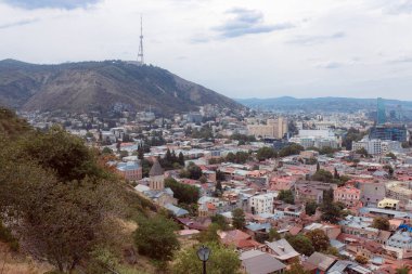 TBILISI, GEORGIA - 9 AĞUSTOS 2021: Dağlık arazili kırmızı tuğlalı evlerin olduğu eski şehir manzarası.