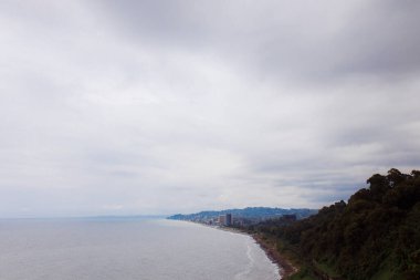 Botanik Bahçesi. Uçurumdan Karadeniz 'e bak. Yoğun yeşil yapraklarla kaplı dağlar. Tren yolu deniz kıyısındaki uçurumdan geçiyor..