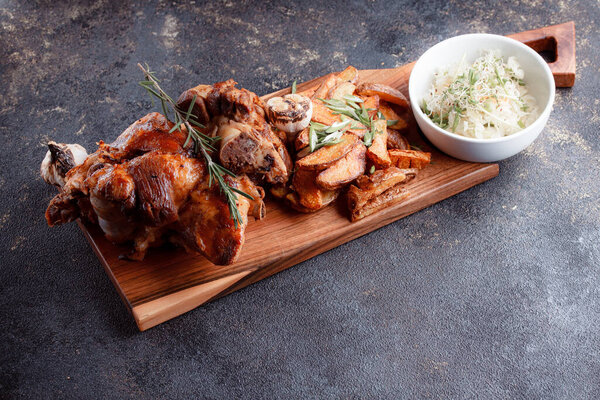 A large piece of fried meat on the bone close-up. Sliced garlic fried on a josper. Grilled potatoes in large chunks.