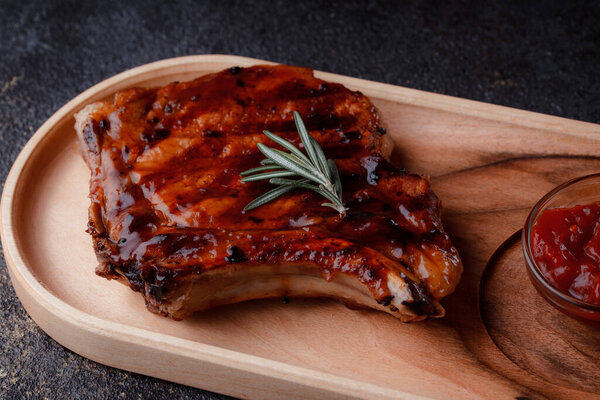 Свиной стейк на гриле в карамельном соусе. Подавать мясо на экологически чистой деревянной посуде. Веточка свежего розмарина и томатный соус.