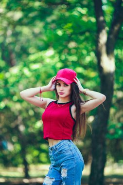 Kırmızı başlık ve konu. Uzun saçlı, güzel ve ciddi bir yüz ifadesi olan kız. Yaz yürüyüşü kıyafetleri. Kişisel bakım kavramı. Yüzünde mutlu duygular.