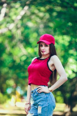 Kırmızı başlık ve konu. Uzun saçlı, güzel ve ciddi bir yüz ifadesi olan kız. Yaz yürüyüşü kıyafetleri. Kişisel bakım kavramı. Yüzünde mutlu duygular.