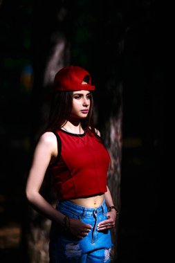 Kırmızı başlık ve konu. Uzun saçlı, güzel ve ciddi bir yüz ifadesi olan kız. Yaz yürüyüşü kıyafetleri. Kişisel bakım kavramı. Yüzünde mutlu duygular.