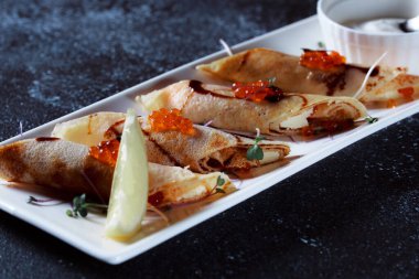 Kırmızı somon havyarlı krep. Koyu mavi arka planda güzel bir yemek servisi. Restoran tatlı menüsü.