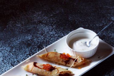 Kırmızı somon havyarlı krep. Koyu mavi arka planda güzel bir yemek servisi. Restoran tatlı menüsü.