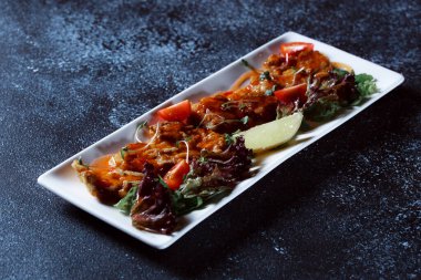 Sebze yahnisi. Bir restoranda haşlanmış sebze servis edilir. Koyu mavi arka planda beyaz plaka.