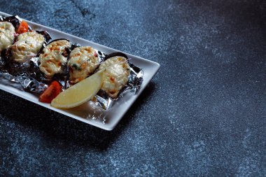 Erimiş peynirli haşlanmış istiridye. Büyük beyaz bir tabakta güzel istiridye servisi. Koyu mavi arka planda bir restoran için hazırlanmış deniz ürünleri..